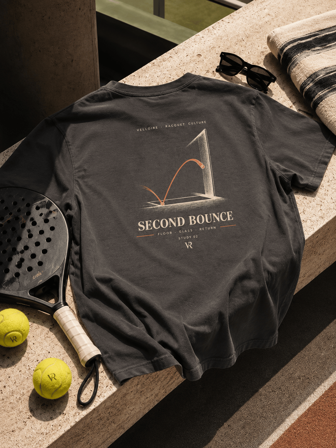 Faded black Second Bounce T-shirt arranged beside a padel racquet and tennis ball