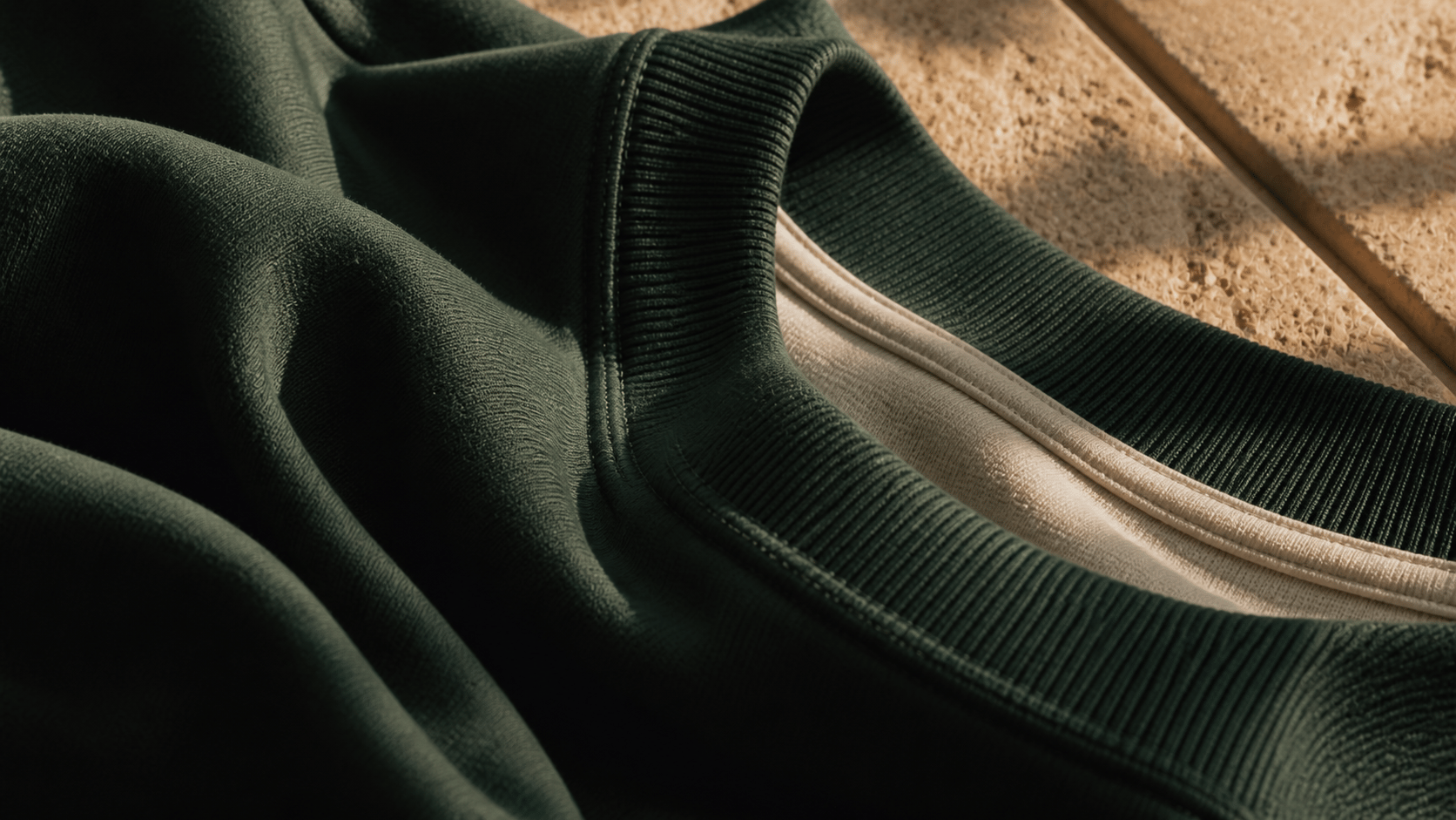 Close detail of forest-green and cream cotton fabric, ribbing, and stitching in sunlight